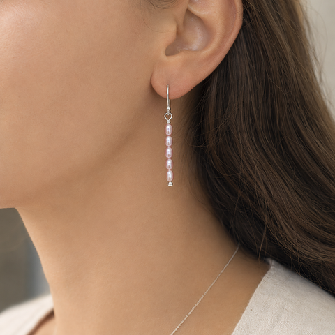 A close-up of a woman's ear wearing a delicate silver dangle earring with five small pink beads, shown against her skin and brown hair by Judy McPhee of Salt Spring Island.