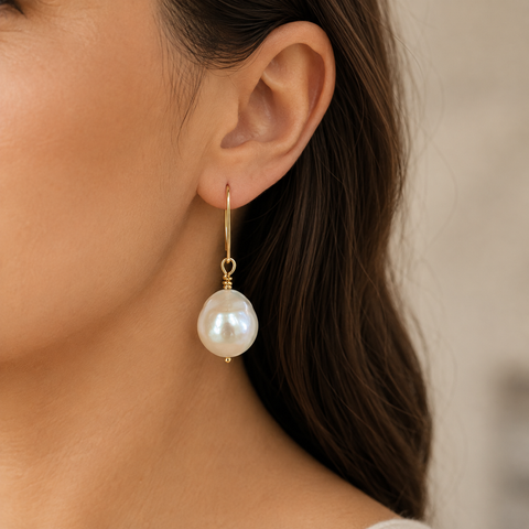 A close-up of a woman's ear wearing a single gold drop earring with a large white pearl pendant by Judy McPhee of Salt Spring.