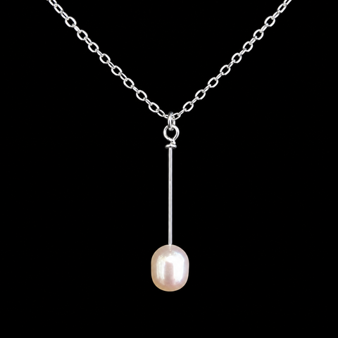 A silver chain necklace featuring a minimalist pendant with a single vertical silver bar suspending an oval, lustrous pearl, set against a solid black background Pearl Necklace by Judy McPhee of Salt Spring Island.
