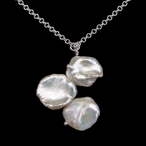 A silver chain necklace featuring three irregular, lustrous baroque pearls in a cascading arrangement, set against a solid black background by Judy McPhee of Salt Spring Island.