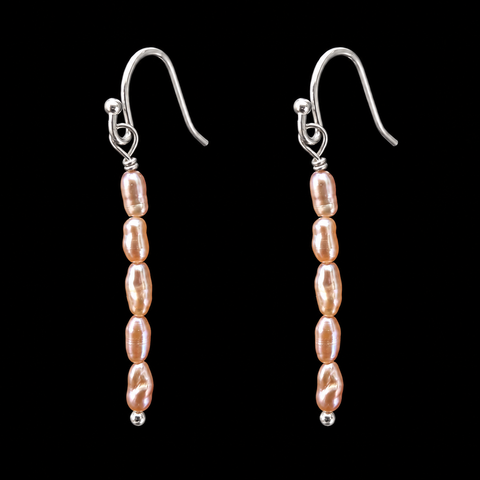A pair of silver fishhook drop earrings with vertical strands of irregular, pearlescent blush pink baroque beads, set against a solid black background.