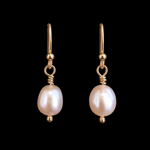A pair of gold drop earrings featuring irregular white freshwater pearls, shown against a solid black background.