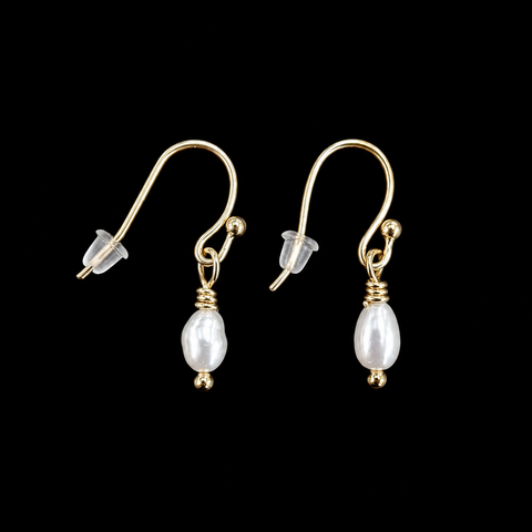 A pair of gold dangle earrings with white baroque pearl drops, shown against a solid black background.