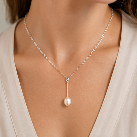 A delicate silver chain necklace with a single vertical drop leading to a round white pearl pendant, shown worn on a model's neck over a light beige V-neck top by Judy McPhee of Salt Spring Island.