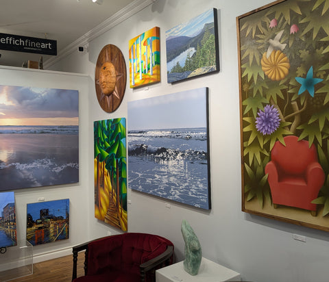 Art gallery with various paintings on the wall and a red chair in the foreground.